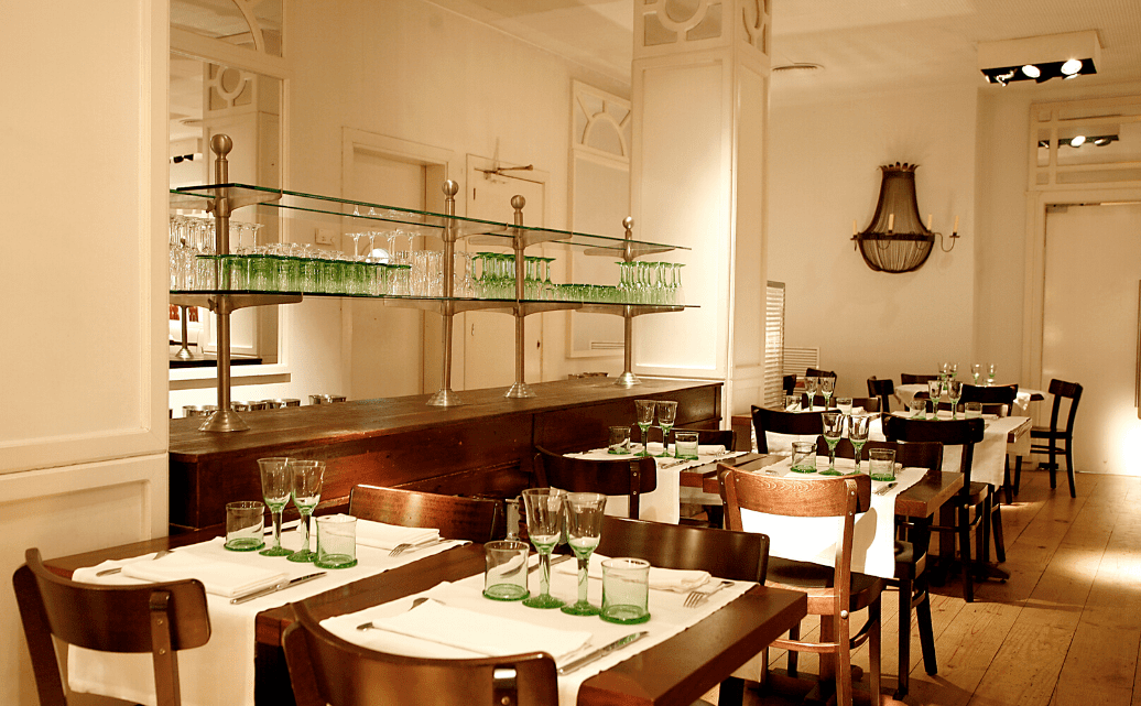 Cocina mediterránea de fusión en local elegante y moderno con vitrinas con botellas de colores en salón blanco en el centro de Girona.                        