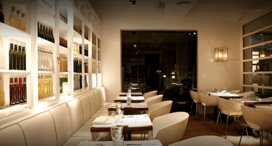 Cocina mediterránea de fusión en local elegante y moderno con vitrinas con botellas de colores en salón blanco en el centro de Girona.                        